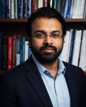 Anirban Acharya headshot in a library setting. 